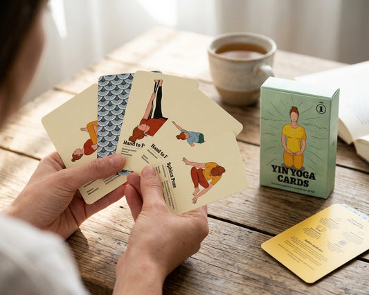 Hand houdt vijf Yin Yoga Cards met houdingen als Sphinx Pose en Hand to Foot, naast de doos van set 1 en de gele uitlegkaart